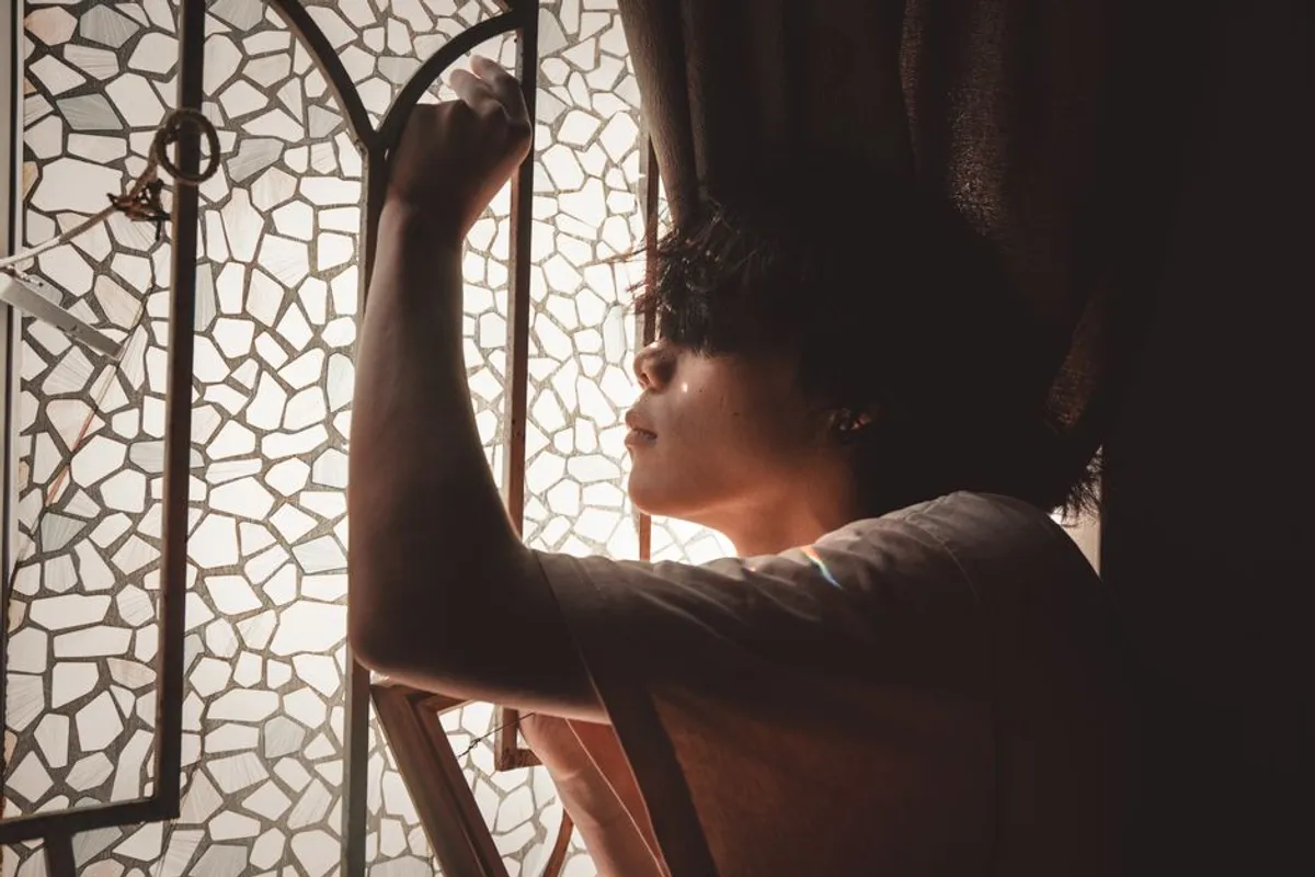 Person sitting alone by a window in quiet, thoughtful light