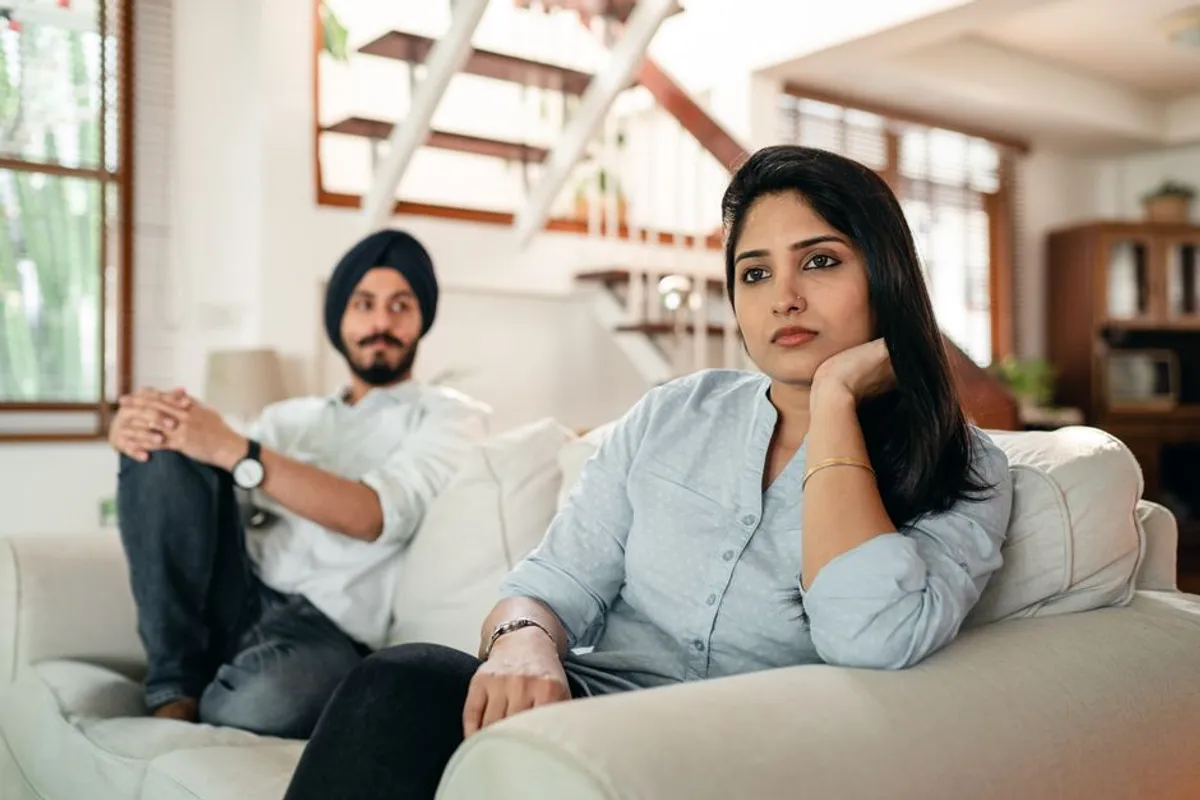 Couple sitting apart on a sofa, tired, in the evening