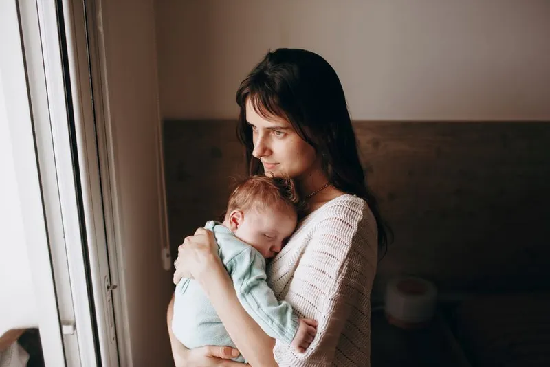 Parent holding a baby at home, looking exhausted