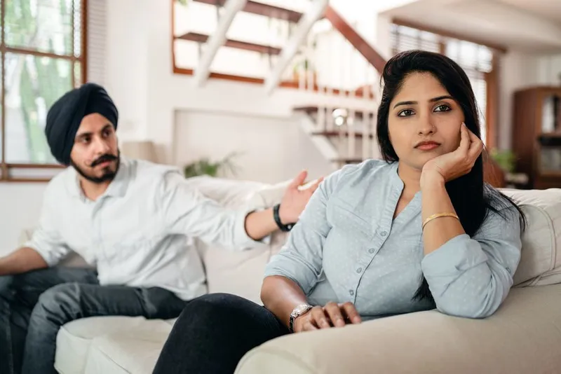 Couple sitting quietly on a sofa, one looking hesitant with a phone